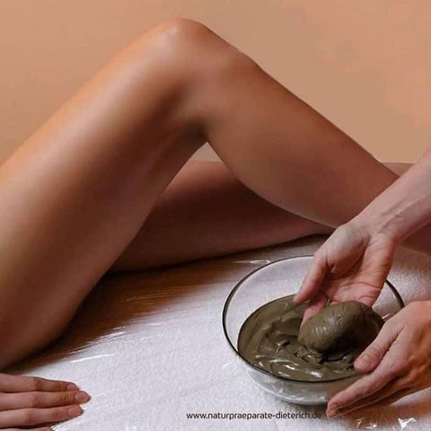 Schüssel mit GUAM Algenfango wird auf Folienunterlage vorbereitet, bevor der Anti-Cellulite-Wickel am Oberschenkel einer liegenden Frau erfolgt. Naturpräparate Dieterich