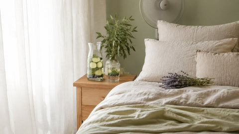 Ruhiges Sommerschlafzimmer mit Leinenbettwäsche, Lavendel und einer Karaffe Sommerwasser.